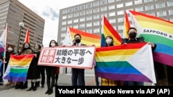 A felperesek ügyvédei és támogatóik szivárványos zászlókkal, valamint az "Alkotmányellenes döntés" feliratú plakáttal állnak Sapporo kerületi bírósága előtt Japánban, 2021. március 17-én.
