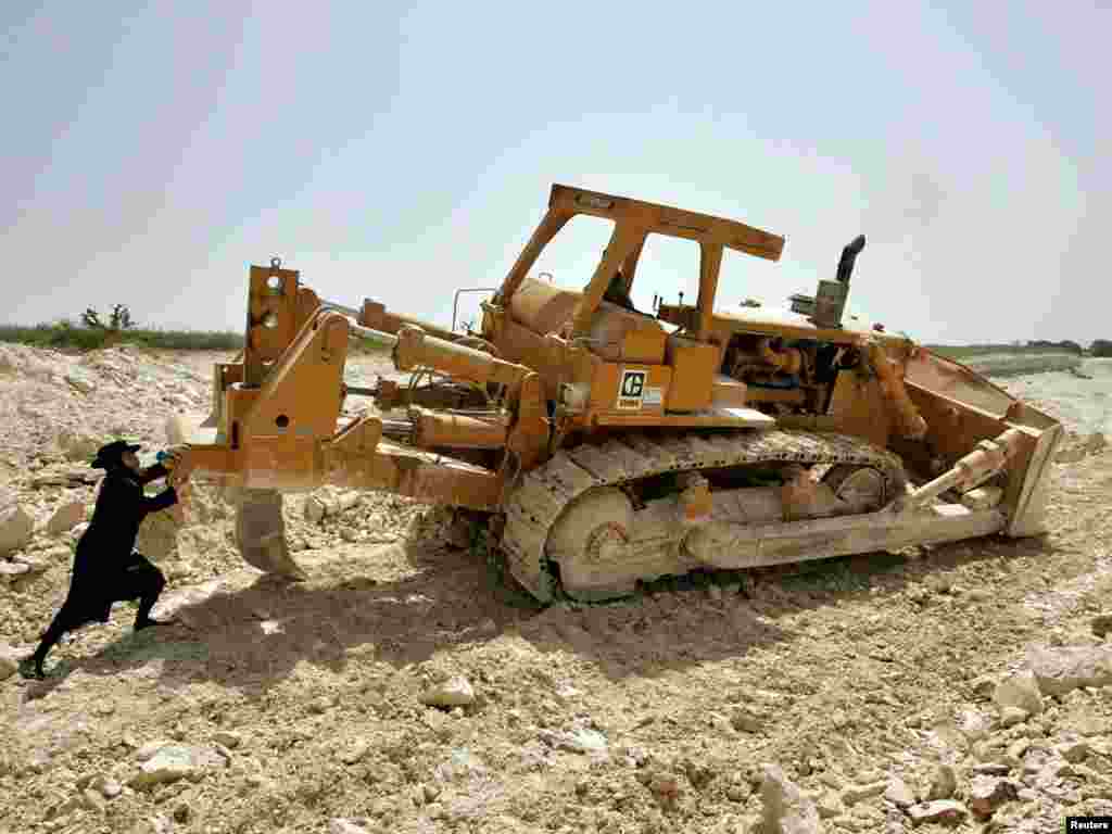 An ultra-Orthodox Jewish protester tries to push a bulldozer at a demonstration against the desecration of graves during the construction of a new Israeli highway next to the northern Israeli Kibbutz of Regavim April 14, 2005. Demonstrators scuffled with security guards during the fourth day of protests against the construction of the highway. REUTERS/Gil Cohen Magen 