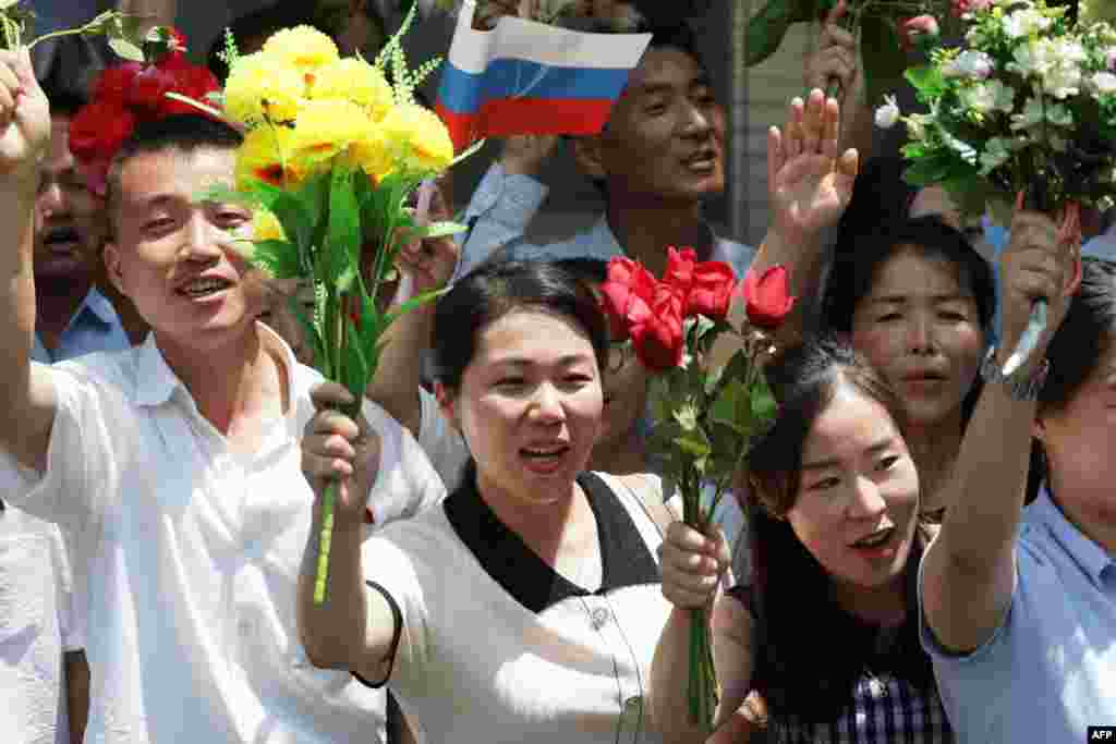 Oameni din Coreea de Nord salută coloana oficială în care se află Putin și Kim, la Phenian, Coreea de Nord,&nbsp;19 iunie 2024.