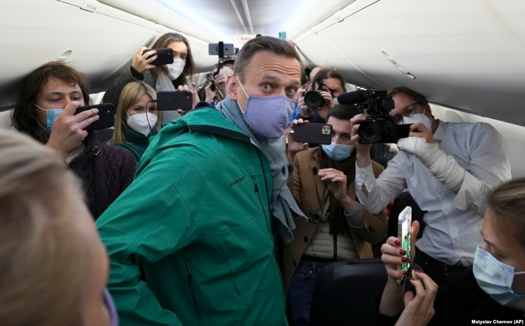 Navalny è circondato da giornalisti all'interno dell'aereo a Berlino prima del suo volo per Mosca il 17 gennaio 2021. Dopo essersi ripreso dall'avvelenamento, Navalny ha deciso di tornare in Russia.  Al suo arrivo a Mosca, è stato arrestato con l'accusa di aver violato i termini della sua libertà vigilata lasciando il paese senza permesso.