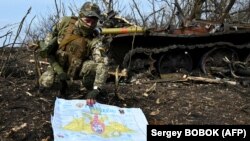 Украинский военнослужащий показывает фотографу российский документ возле сожженного танка вблизи села Мала Рогань к востоку от Харькова, 1 апреля 2022 года