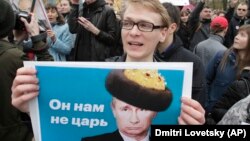 Демонстранты несут плакаты с изображением президента России Владимира Путина во время акции протеста в Санкт-Петербурге, Россия, 5 мая 2018 года