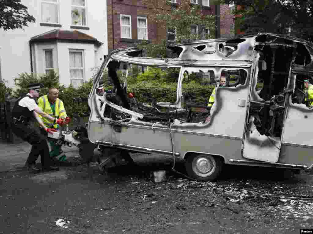 A police officer helps council workers to move the burned-out shell of a camper, which was torched during overnight rioting and looting in the neighbourhood of Toxteth in Liverpool, northern England, on August 10. Photo by Phil Noble for Reuters