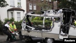 A police officer helps council workers move the burned-out shell of a camper, which was torched during overnight rioting and looting in the neighborhood of Toxteth in Liverpool.
