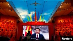 Visitors stand in front of a giant screen displaying Chinese President Xi Jinping next to a flag of the Communist Party of China at the Military Museum of the Chinese People's Revolution in Beijing.