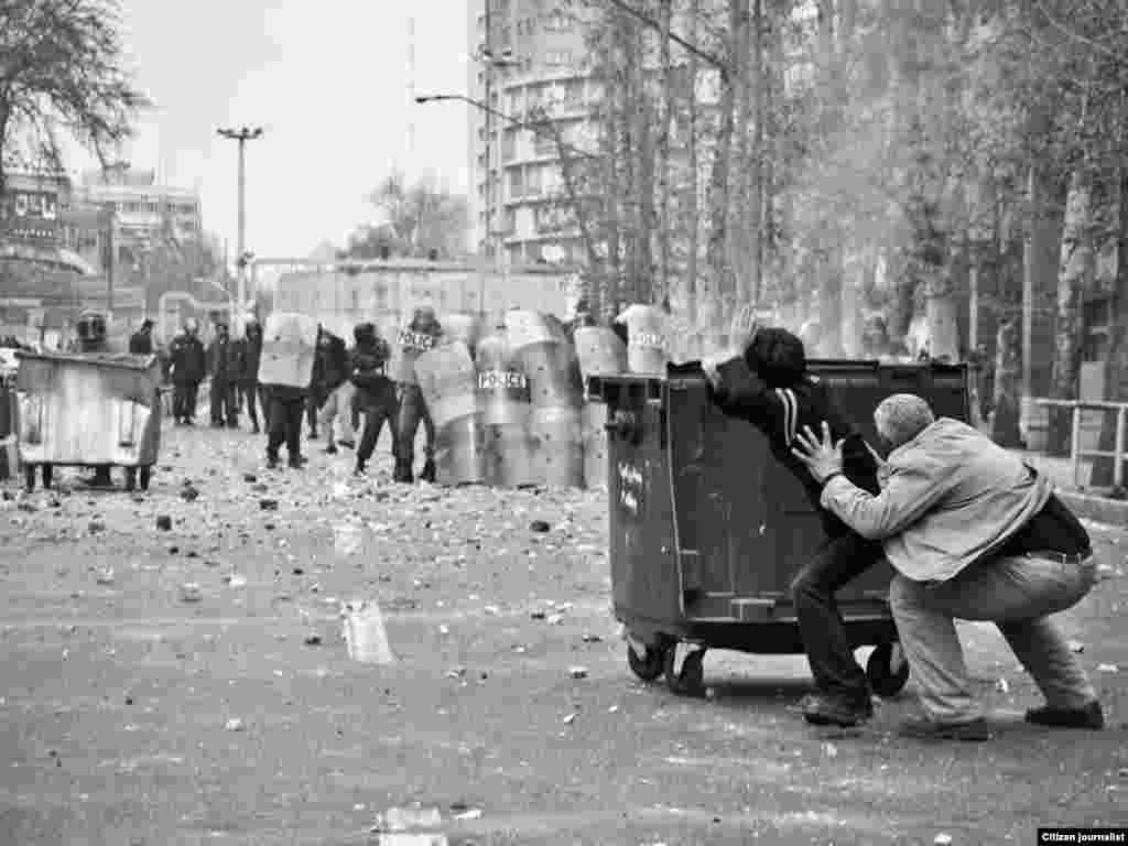 Iran -- Two men hide behind a dustbin from riot policemen during clashes in Tehran on December 27, 2009.