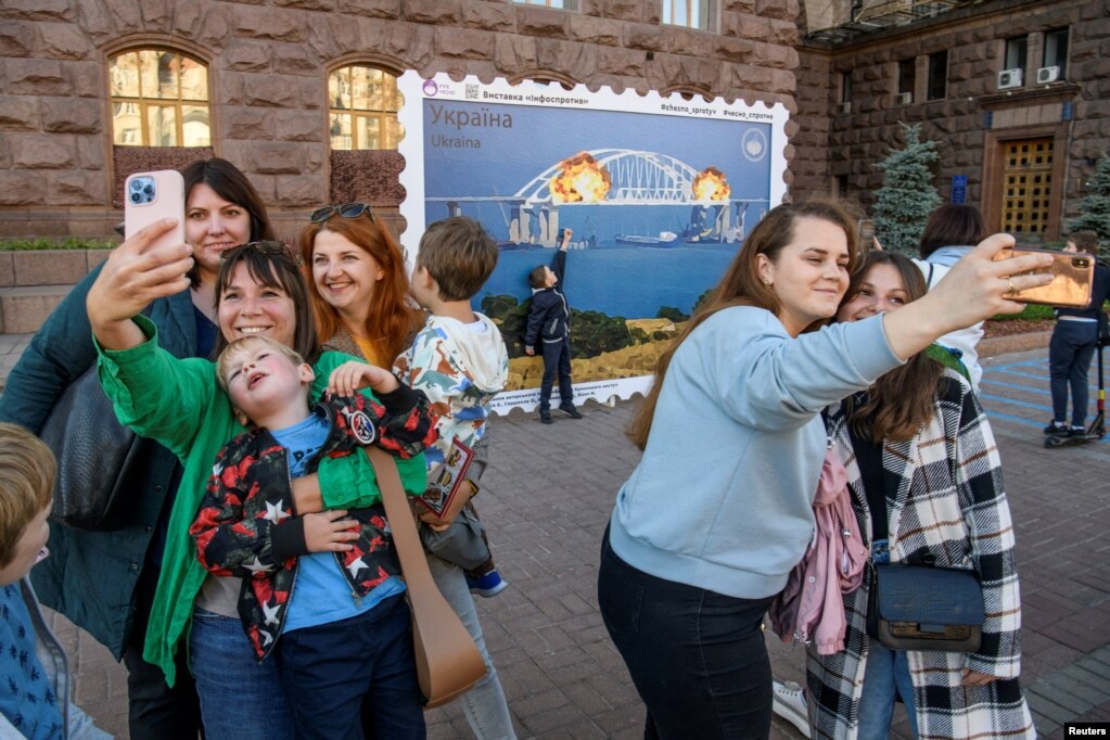 Njerëzit fotografohen në Kiev përpara një fotografie me përmasa më të mëdha ku shihet në zjarr Ura e Krimesë. &nbsp;