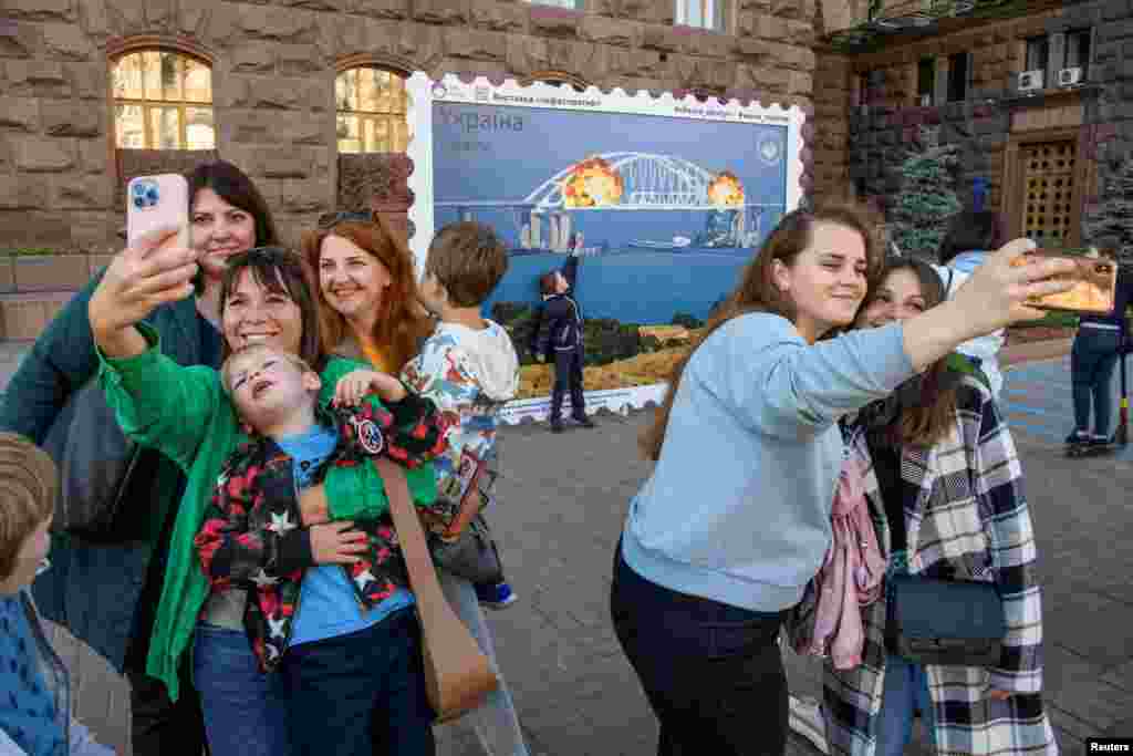 People take selfies in front of a Kyiv artwork depicting the Crimea Bridge on fire.