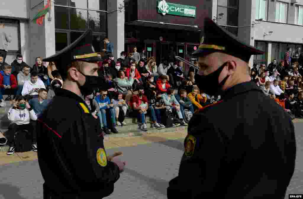 Belarusian policemen watch as students stage a sit-in protest near the entrance of their university.