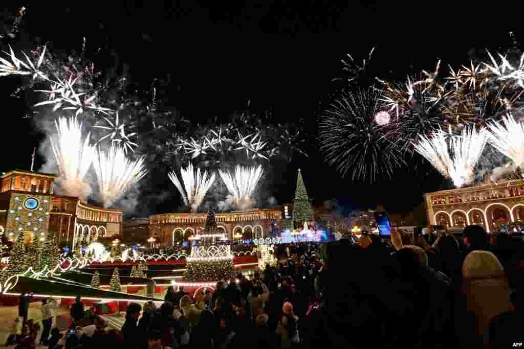 Oamenii privesc focurile de artificii care luminează cerul deasupra orașului Erevan, în timpul ceremoniei de aprindere a bradului de Crăciun, pe 14 decembrie 2025.
