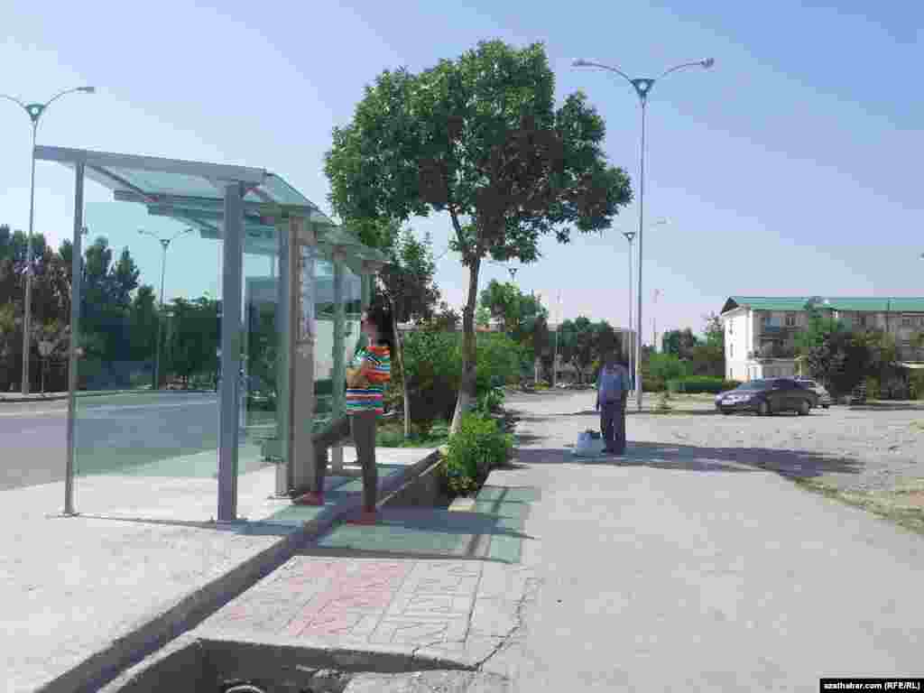 Awtobus duralgasynyň kölegesinde awtobusa garaşyp duran bir gyz.