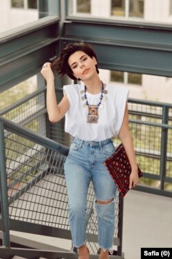 Safia pairs her simple t-shirt and jeans with an Afghan tribal coin necklace, originating from the Kuchi nomads of Afghanistan. She adds a red Afghan rug inspired clutch to finish her east meets west look.