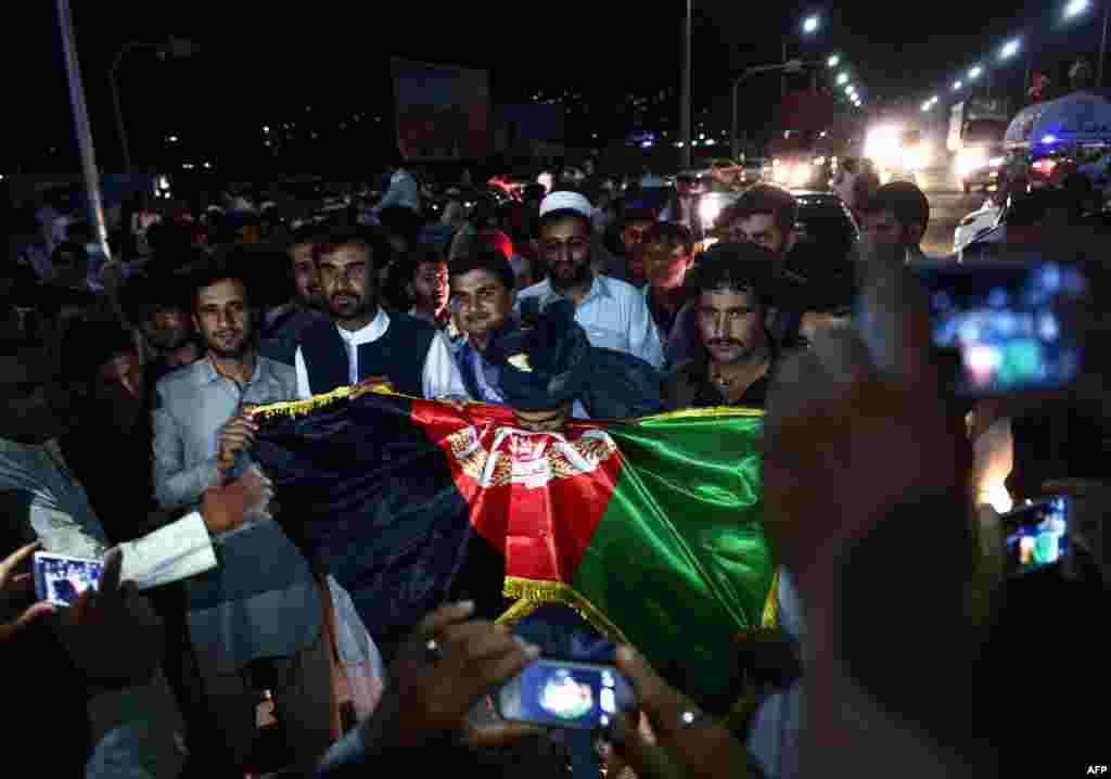 A man poses for photos holding an Afghan national flag as supporters of presidential candidate Ashraf Ghani celebrate in the street after preliminary election results showed he won on July 7 in Kabul. (AFP/Wakil Kohsar)