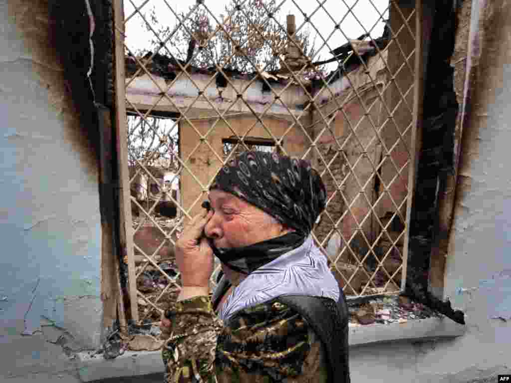 Kyrgyzstan -- An ethnic Uzbek woman cries as she passes by a burnt-out house in the town of Osh, 24Jun2010 - KYRGYZSTAN, Osh : An ethnic Uzbek woman cries as she passes by a burnt-out house in the town of Osh on June 24, 2010. Almost all the refugees who fled Kyrgyzstan during ethnic clashes and crossed the border into Uzbekistan have now returned, the deputy head of the country's border service said.