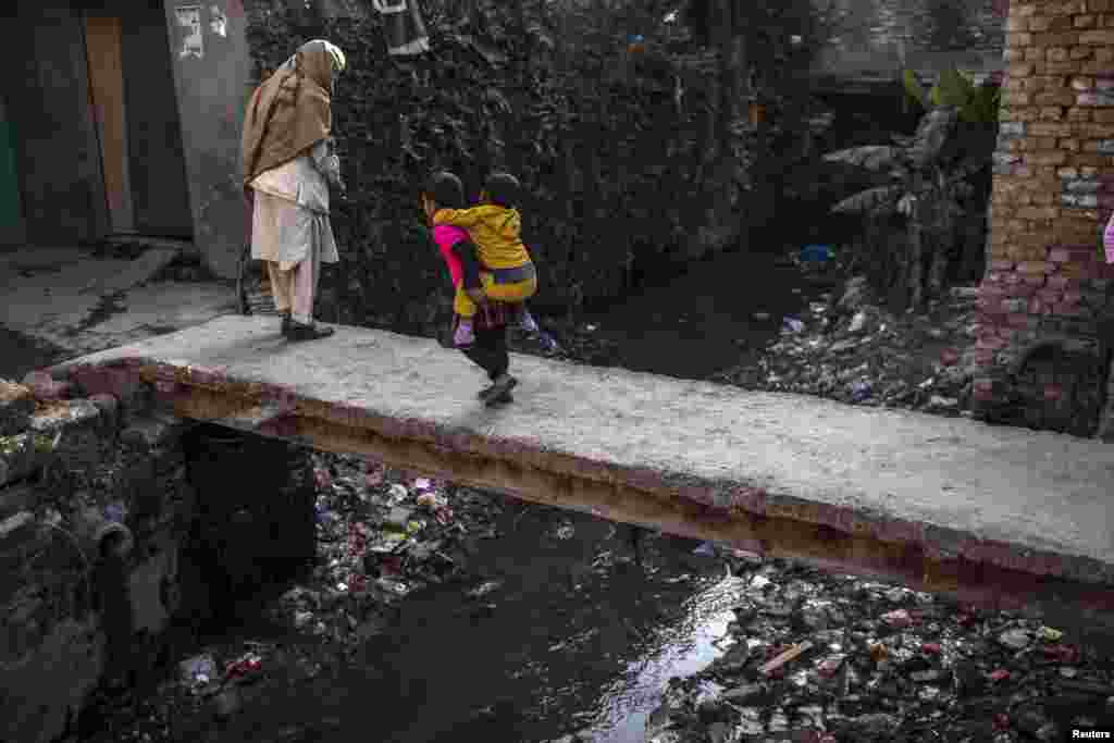 A 7-year-old Pakistani girl carries her younger sister on her back while she walks in a Christian slum in Islamabad. (Reuters/Sara Farid)