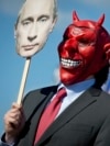 Germany -- An activist wears a devil's mask which he covers with a picture of Vladimir Putin as part of a protest against the Russian President outside the congress center of the Hanover trade fair on in Hanover, 07Apr2013