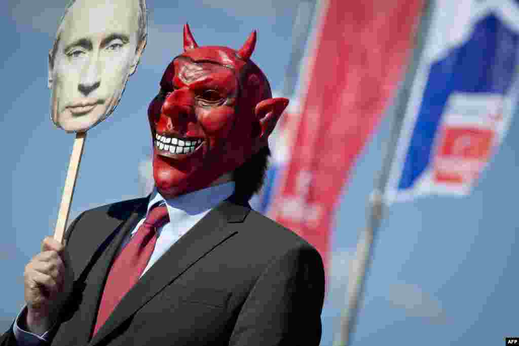 An activist wears a devil&#39;s mask that he covers with a picture of Vladimir Putin as part of a protest against the Russian president outside the congress center of the Hanover trade fair on in Hanover. (AFP/Odd Andersen)