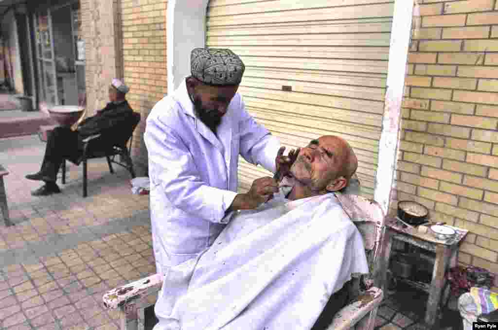 A man receives a shave from a street barber. - Kashgar's old city has survived the centuries, and remains an important Islamic cultural center for the Uyghurs, the Turkic ethnic group living in Xinjiang Province.