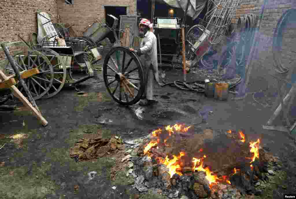A worker burns waste rubber and cow-dung cakes for heat as he repairs wheels for carts pulled by livestock in Peshawar, Pakistan. (Reuters/Khuram Parvez)