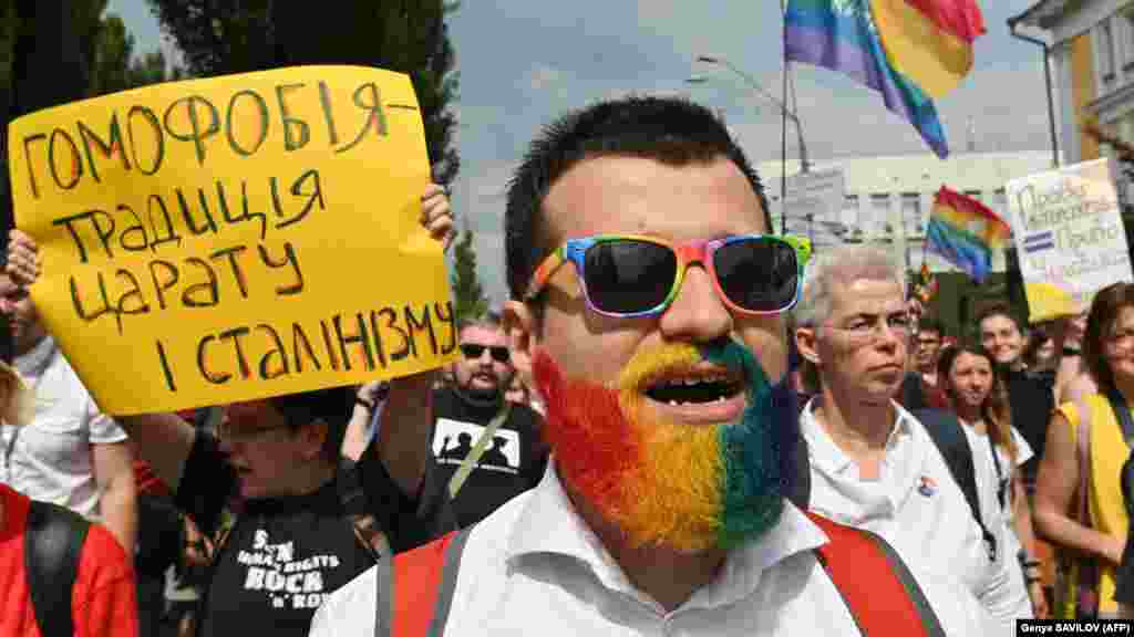 A participant with his beard painted in the rainbow flag colors chants slogans as another holds a placard reading &quot;Homophobia is a Stalinist-era tradition.&quot;