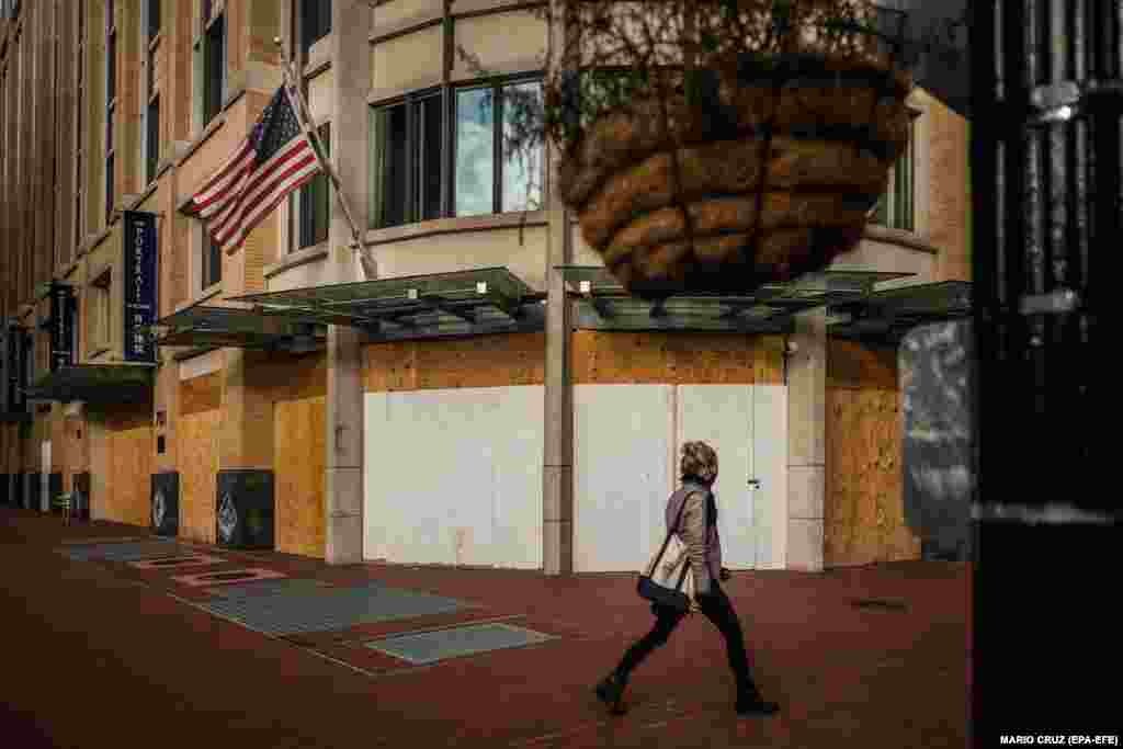 Една жена поминува низ продавница заштитена со дрвени табли во Вашингтон.