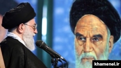 علی خامنه‌ای در مقابل پوستری از روح‌الله خمینی، بنیانگذار جمهوری اسلامی