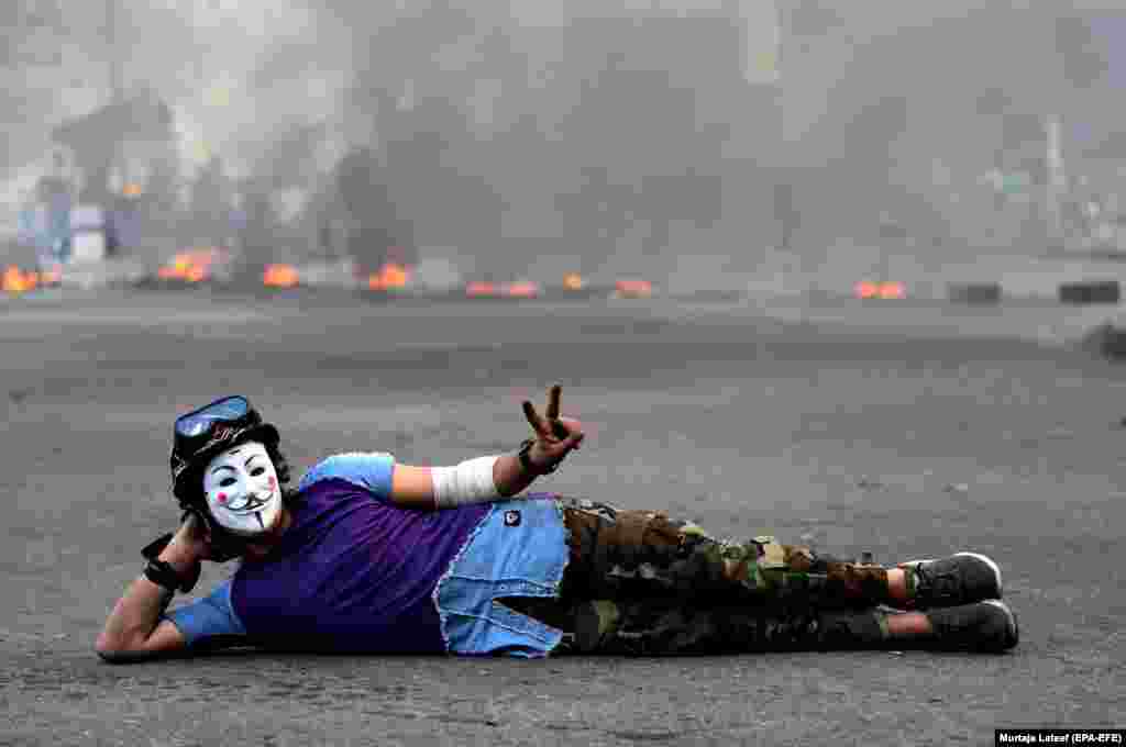 An Iraqi protester wearing a Guy Fawkes mask flashes victory signs during a protest and strike in a central Baghdad square. (epa-EFE/Murtaja Lateef)&nbsp;