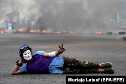 An Iraqi protester wearing a Guy Fawkes mask flashes victory signs in front a fire set by protesters to block a street during a protest and strike at Khillani square in central Baghdad, November 4, 2019