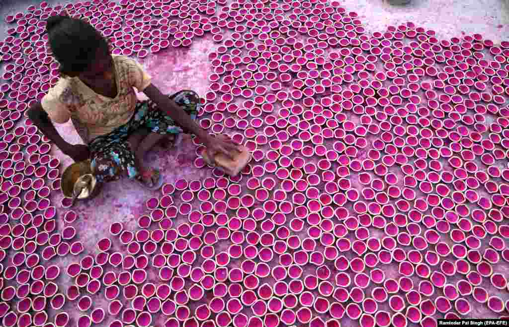 An Indian girl arranges freshly painted "Diya" or earthen lamps for drying at her family's home workshop in Amritsar. (epa-EFE/Raminder Pal Singh)