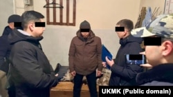 Пара алууга шектелип кармалган милиция кызматкери (ортодо).  УКМК тараткан сүрөт.