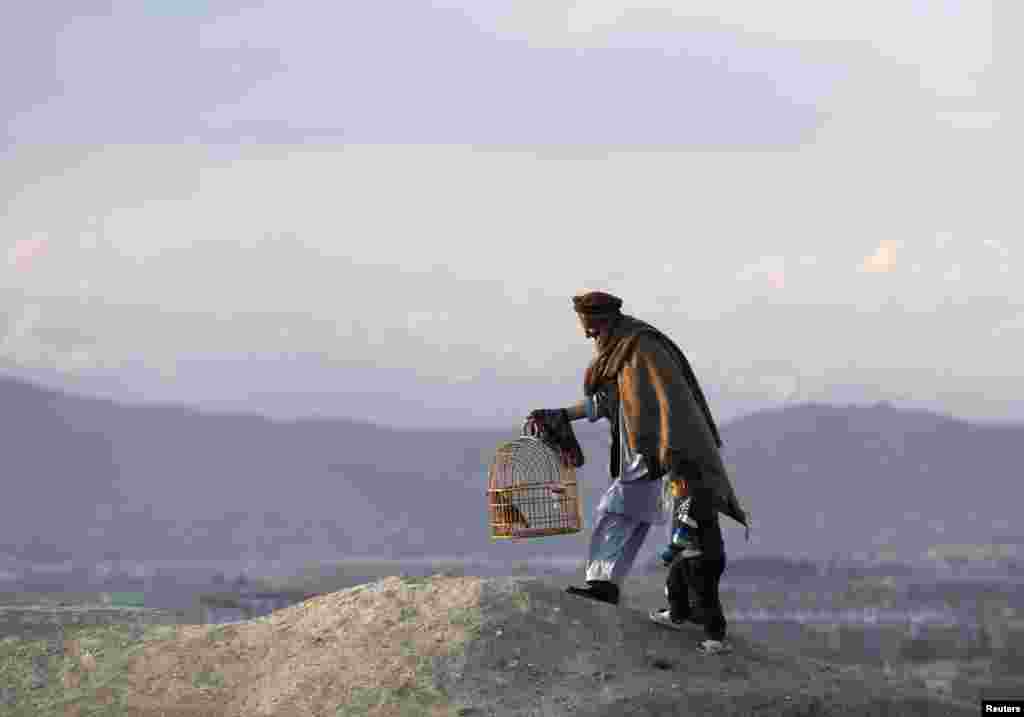 An Afghan man holds onto a child as he walks with a cage of quails on a hill in Kabul on April 23. (Reuters/Mohammad Ismail)