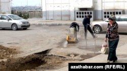 Aşgabadyň Parahat etrapçasynda gazuw işlerini geçirýän işgärler we köçeden geçip barýan zenan.