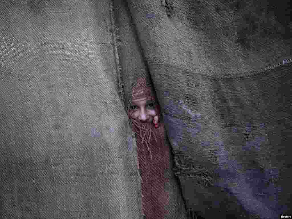 A Pashtun girl peeps through a jut sack from the doorway to her family dwelling in Peshawar, Pakistan on June 1. Photo by Fayaz Aziz for Reuters 