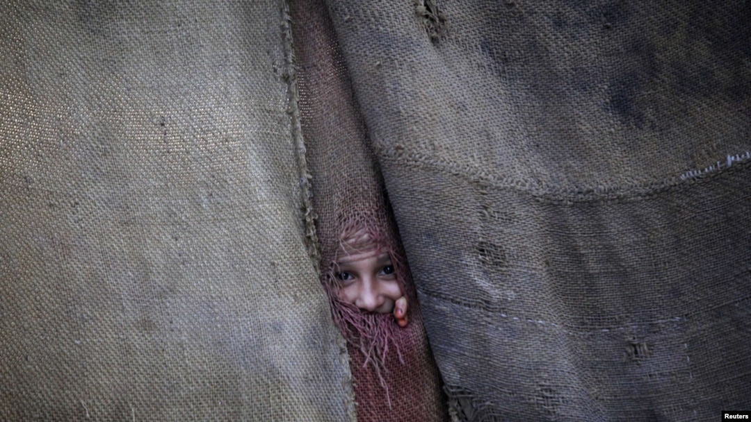 A Pashtun girl peeks through the doorway to her family dwelling in Peshawar.