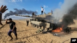 Palesztinok ünnepelnek egy megsemmisült izraeli tank mellett a Gázai övezet kerítésénél 2023. október 7-én