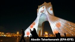 People walk past Azadi (Freedom) Tower lit up with messages of hope in solidarity with all the countries affected by the COVID-19 coronavirus pandemic, in Tehran, March 31, 2020