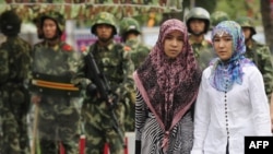 Two Uyghur women pass Chinese paramilitary policemen standing guard outside the Grand Bazaar in Urumqi.