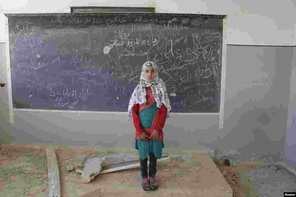 Malak, a 13-year-old girl, poses for a picture inside her damaged classroom at a school used as a military camp for forces loyal to Syria's President Bashar al-Assad, in the rebel-controlled town of Ain Qurei. (Reuters/Khalil Ashawi)