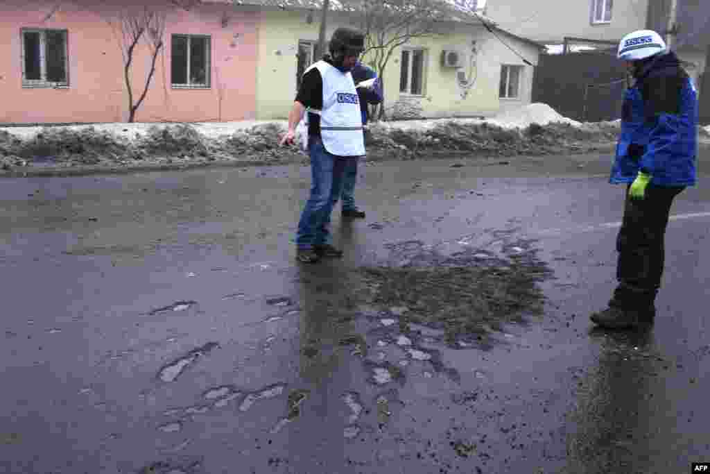 OSCE monitors examine the impact of a shell that hit a residential area in Donetsk&#39;s Kyibishevsky district.