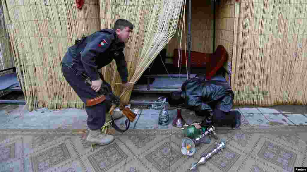 Polisiýa ofiserleri Kabulda bir kafä reýd geçirip, onuň içinden suwly çilim enjamlaryny gözleýärler. (Reuters/Mohammad Ismail)
