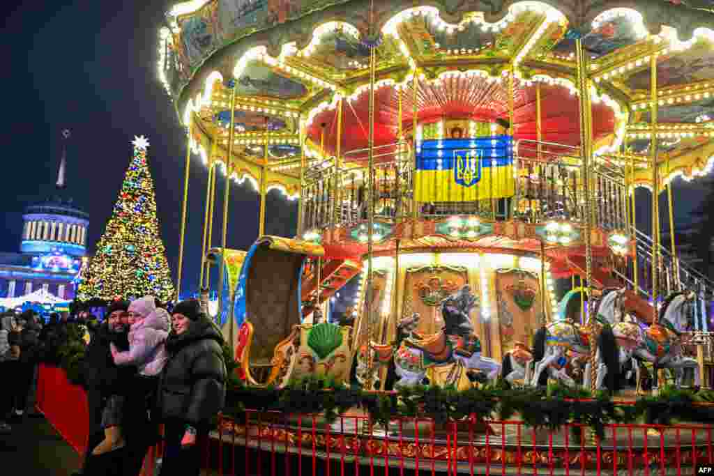 O familie își face o fotografie lângă un carusel în timpul Târgului de Crăciun de la Centrul Național de Expoziții al Ucrainei din Kiev, pe 21 decembrie 2025.