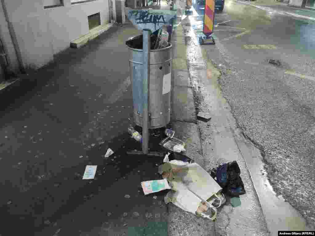 Coș de gunoi aproape gol, dar cu gunoi pe lângă el - la Piața Universității