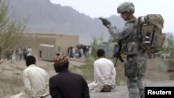Afghanistan -- A US soldier stands guard next to detained Afghan men in the Arghandab valley in Kandahar province, 26Feb2010