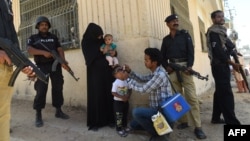 Карачи. Полицейские охраняют сотрудника службы здравоохранения, делающего прививку от полиомеилита ребенку, на следующий день после того, как было совершено нападение на медработника 