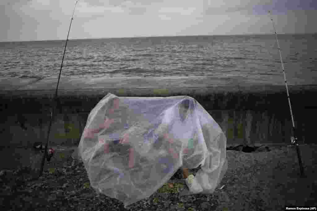 Engelbert Cañete (left) and his friend Ethian Jesus protect themselves from the rain with a plastic sheet while trying to fish in Havana. (AP/Ramon Espinosa)