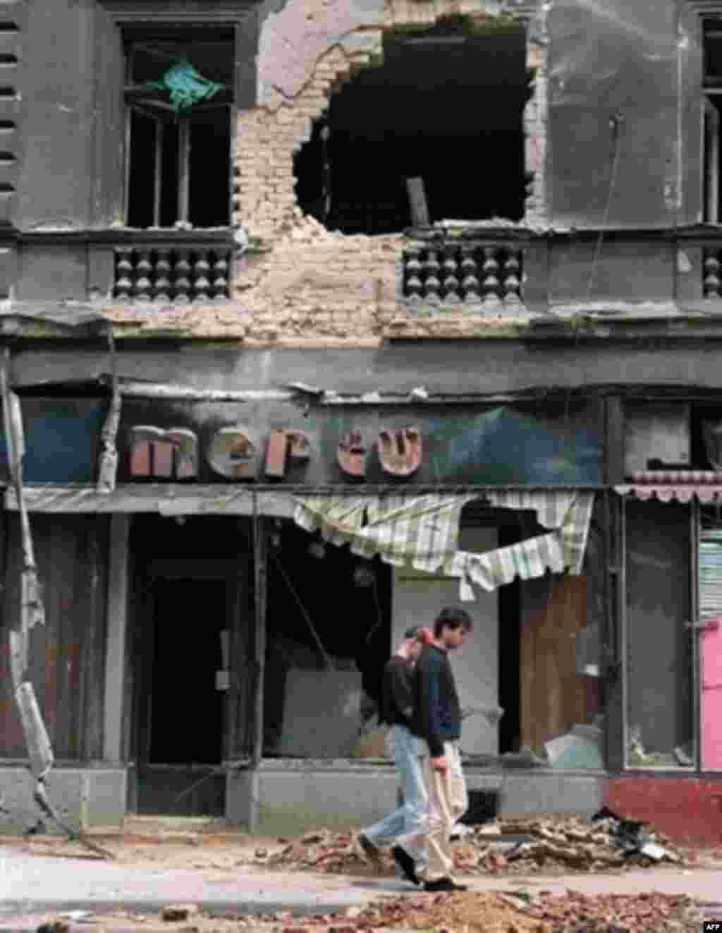 Two residents of Sarajevo walk past a destroyed building on Marshal Tito Avenue in June 1992 - The UN's International Criminal Tribunal for the former Yugoslavia has charged Karadzic with being responsible for his army's shelling of parts of Sarajevo and attacks on civilians during a 43-month siege of the city, during which thousands were killed or wounded.