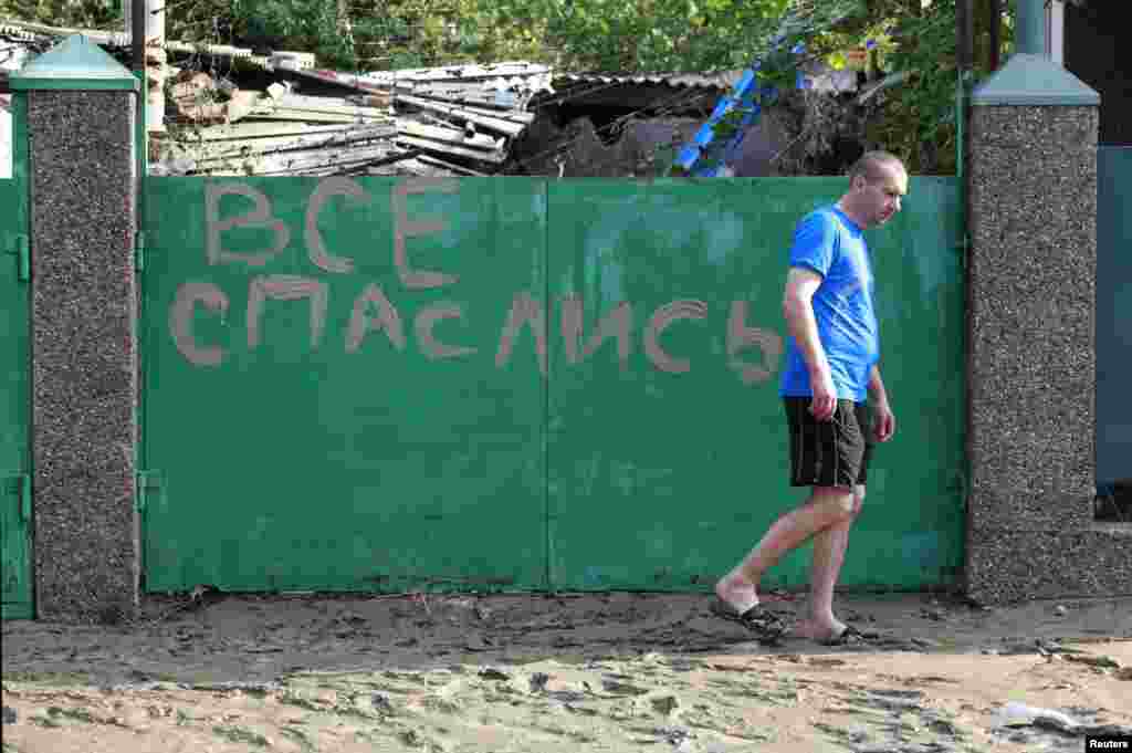 A local resident walks in mud from the floods in the town of Krymsk past a sign reading "Everyone has escaped (found salvation)."