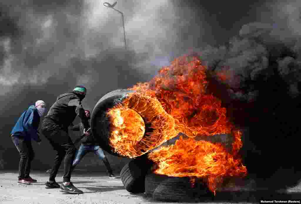 A Palestinian protester moves a burning tire during clashes with Israeli troops near the Jewish settlement of Beit El in the Israeli-occupied West Bank on March 27. (Reuters/Mohamad Torokman)