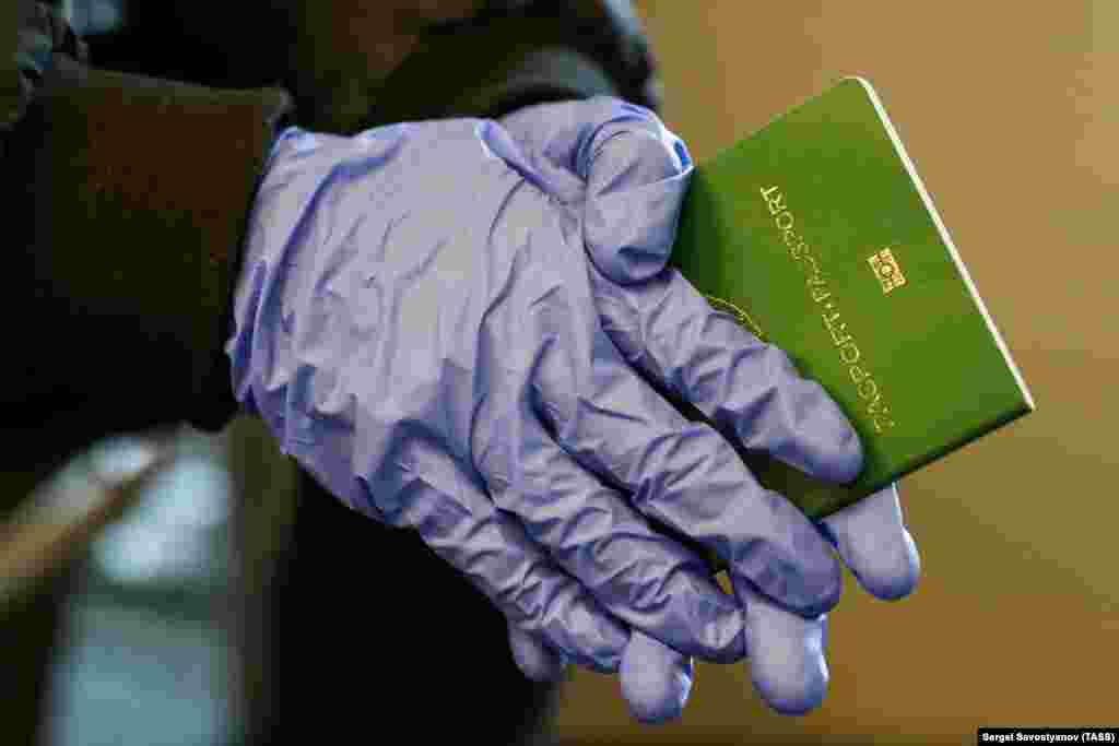 A traveler with gloves and an Uzbek passport waits at Vnukovo International Airport on March 25.