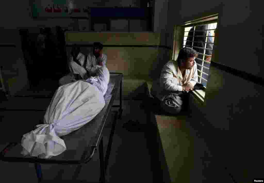 Karachi residents sit beside the body of a dead relative while waiting for an ambulance at a city morgue.&nbsp;